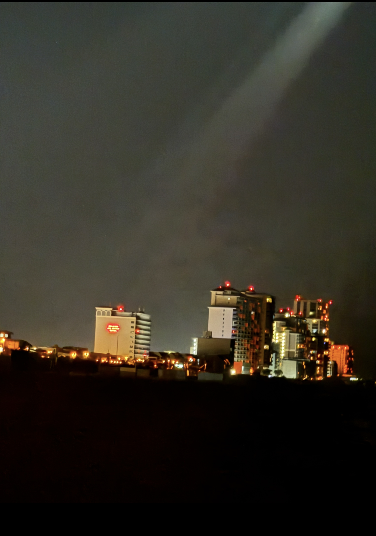 The same arm of light, framed lower to include the beachfront skyline beneath it